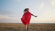 © maxximmm - girl with the cloak. concept of a happy childhood and family for a child. a little girl in a superhero costume runs across a field, a red cape and a blue T-shirt, sunset on the background lifestyle