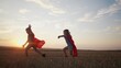 © maxximmm - children in superhero costumes. concept of a happy childhood and family for a child. a boy and a girl with red capes and blue T-shirts are running across a field, sunset in the lifestyle background