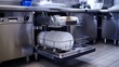 © horizon - A commercial kitchen dishwasher machine with its door open, displaying clean plates and cutlery, highlighting the role of industrial cleaning equipment in food service settings.