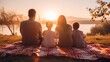 © tohceenilas - A family of four enjoying a serene sunset picnic by the lake, spending quality time together on a blanket in nature.