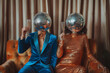 © ALL YOU NEED studio - couple with disco ball heads sitting on the  couch, blue and orange tones, festive , curtain background, retro party vibes, surreal 70s  theme, funky holiday card with copy space and motion blur
