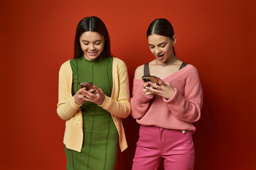 Two pretty, brunette teenage girls stand together, absorbed in their cell phones, ignoring their surroundings.