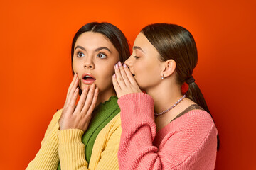 two pretty, brunette teenage girls in casual attire stand next to each other with mouths open in sur