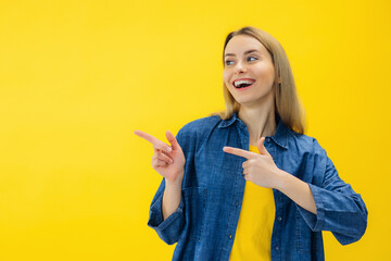 Positive woman smiles positively recommends using blank space indicates at upper left corner dressed in casual wear over vivid yellow background shows direction or way