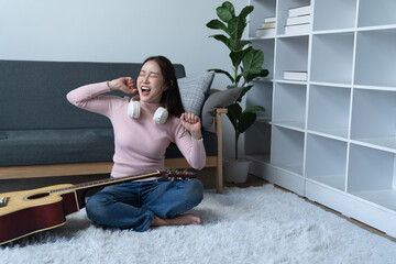 weekend day asian girl is sitting on couch blowing off steam by singing playing guitar at home. woman holding microphone with exaggerated body movement is having happy and crazy time alone.