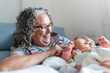 © Raul Navarro/Stocksy - A smiling elderly woman cradling a newborn in a cozy room.