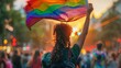 © yailek - The image shows a person waving a rainbow flag at a pride parade. The flag is a symbol of the LGBTQ+ community, and the parade is a celebration of the diversity of the community.