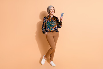 Sticker - Full length photo of smart pleasant person wear print blouse pants look at smartphone arm in pocket isolated on beige color background