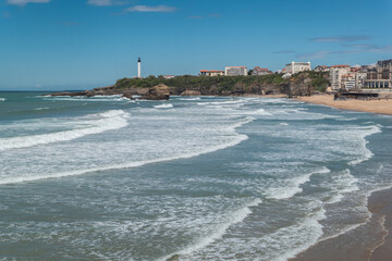 A encantadora costa de Biarritz com as ondas suaves e o farol solitário sobre o penhasco ao fundo