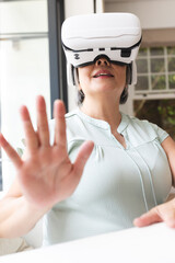 Wall Mural - A senior Asian woman wearing virtual reality headset at home, reaching out