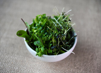 Wall Mural - Green salad in a cup on a burlap cloth. Herbal salad on a yellow background.