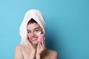 Wall Mural - Young woman washing face with brush and cleansing foam on light blue background. Space for text