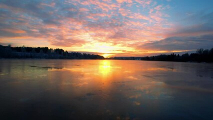 Wall Mural - Drone shot of a frozen lake in a forest with a scenic cloudy dusk sky in the background