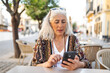 © Lupe Rodríguez/Stocksy - white-haired woman sitting in a cafe looking at her mobile phone