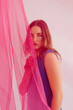 © Tania Cervian/Stocksy - Serious female model standing behind transparent pink fabric