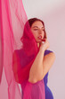 © Tania Cervian/Stocksy - Pensive young lady in bodysuit standing behind pink veil