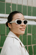 © Azamat Mukanov/Stocksy - Asian woman in sunglasses poses against a green wall background