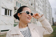 © Azamat Mukanov/Stocksy - Woman in sunglasses against the background of an apartment building
