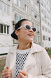 © Azamat Mukanov/Stocksy - Woman in sunglasses against the background of an apartment building