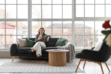 Poster - Young woman using mobile phone on sofa near window in living room