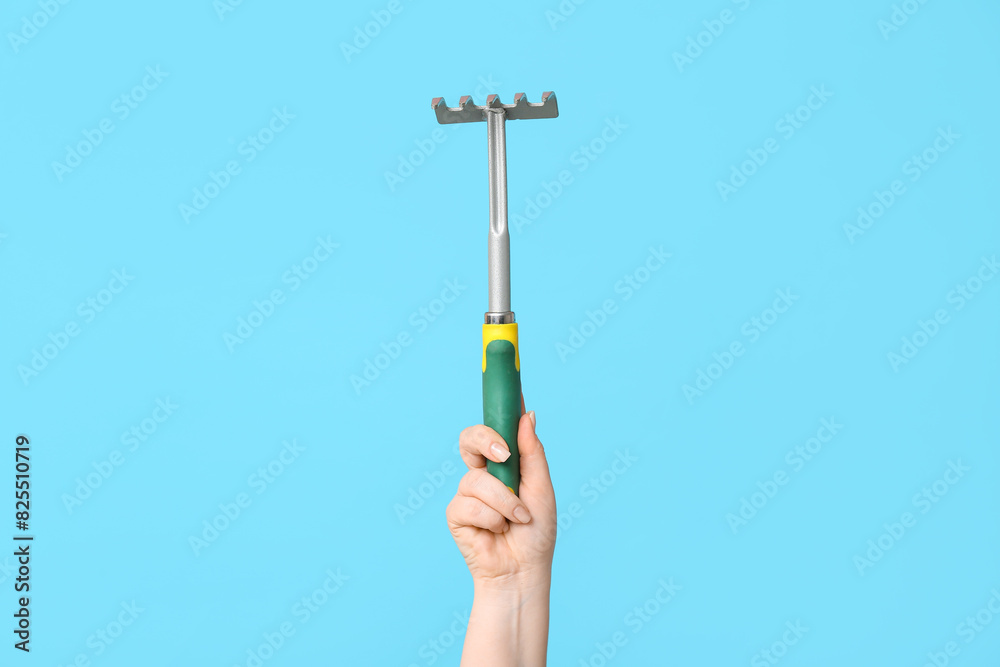 Female hand with gardening rake on color background, closeup