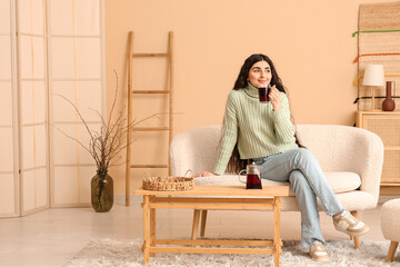 Sticker - Beautiful young woman with glass cup of hot tea on sofa in living room