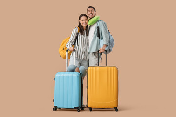 Wall Mural - Beautiful young happy couple of tourists with suitcases, backpacks and travel pillows on brown background