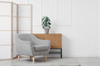 © Pixel-Shot - Interior of light living room with grey armchair, chest of drawers and folding screen near white wall