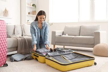 Female Asian traveler with organizers packing suitcase at home