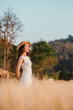 © Satori Studio - A woman in a white dress stands in a field of tall grass. She is wearing a straw hat and smiling. The scene is peaceful and serene, with the woman looking out over the grassy field