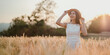 © Satori Studio - A woman is standing in a field of tall grass, wearing a straw hat and smiling. Concept of freedom and relaxation, as the woman is enjoying her time in the open field