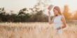 © Satori Studio - A woman is standing in a field of tall grass, wearing a straw hat and a white dress. She is smiling and she is enjoying the outdoors. Concept of freedom and relaxation
