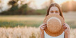 © Satori Studio - A woman is holding a straw hat and is hiding her face behind it. The image has a light and playful mood, as the woman is posing with the hat and making a silly face