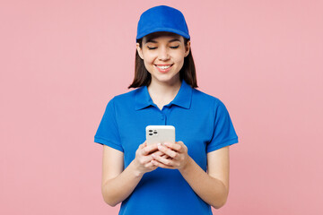 Wall Mural - Professional smiling delivery girl employee woman wear blue cap t-shirt uniform workwear work as dealer courier hold in hand use mobile cell phone isolated on plain pink background. Service concept.