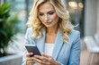 © Юлия Клюева - A blonde businesswoman with curly hair. She is dressed in a casual blue jacket. In the hands of a smartphone. A businesswoman looks at her mobile phone.