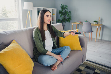 Wall Mural - Full length portrait of nice young girl hold tv remote sit sofa wear green shirt modern interior flat indoors