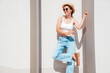 © halayalex - Beautiful smiling model in sunglasses. Female dressed in summer hipster white T-shirt and jeans. Posing near white wall in the street. Funny and positive woman having fun outdoors, in hat, sunglasses