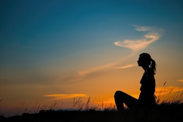 Poster - A silhouette of a woman sitting in a field at sunset. Perfect for nature and relaxation concepts