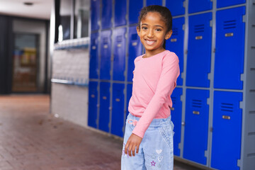 Wall Mural - In school, young biracial girl is standing by blue lockers with copy space