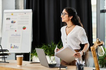 Wall Mural - Young indian woman in glasses working at desk with laptop.