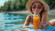 © Александр Марченко - A smiling woman in a hat and sunglasses enjoying a refreshing drink with orange slices by the water.