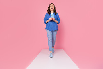 Poster - Full body photo of attractive retired woman walk podium hold device dressed stylish blue clothes isolated on pink color background