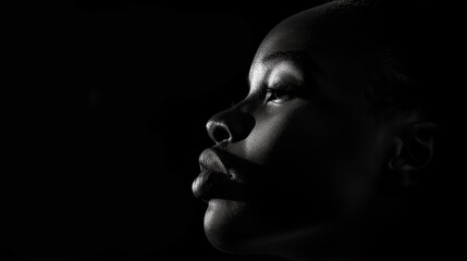 Dramatic black and white profile portrait of a woman with strong facial features, highlighted by intense lighting against a dark background, emphasizing the texture and contours of the face