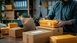 © Oulaphone - A man preparing packaging for delivery, with boxes and a laptop on the table, working in an e-commerce or online marketing business concept.
