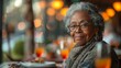 © Prostock-studio - A woman is seated at a table, holding a glass of orange juice in a senior living community cafe.