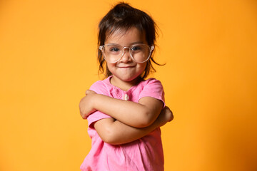 Wall Mural - A young child with a confident smile, The child is wearing a pink shirt and large, clear-rimmed glasses. They have their arms crossed over their chest in a playful and self-assured manner