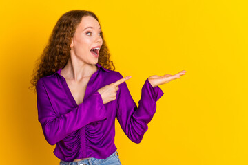 Poster - Photo portrait of lovely young lady look amazed point hold empty space dressed stylish violet garment isolated on yellow color background