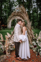 Riga, Latvia, - August 26, 2023 - A bride and groom share a kiss during their outdoor wedding ceremony, surrounded by decorative plants and greenery.