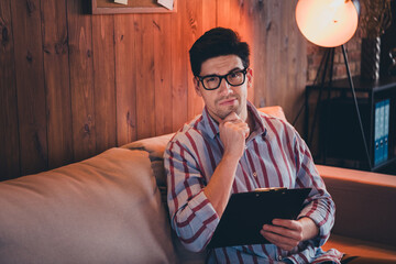 Poster - Photo of successful young corporate man sit sofa think hold clipboard lamp light loft interior office home indoors