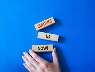 Sticker - Contact us now symbol. Wooden blocks with words Contact us now. Beautiful blue background. Businessman hand. Business and Contact us now concept. Copy space.